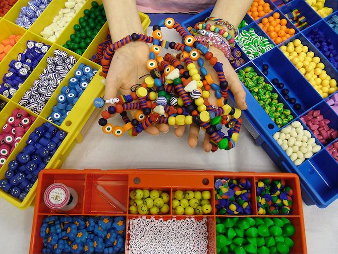 Kinderhände halten selbstgebastelte Ketten mitten Boxen mit bunten Perlen