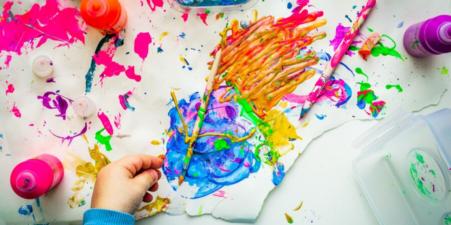 Kinderhand mit Pinseln und bunten Farbklecksen