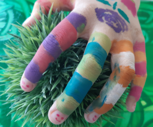 Bunt bemalte Kinderhand greift in grüne Wiese